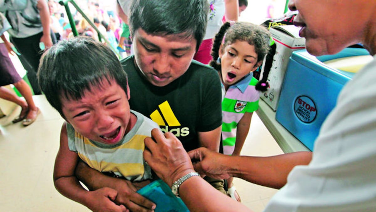 Una niña no puede disimular su sorpresa al ver cómo vacunan al niño formado en la fila por delante de ella.