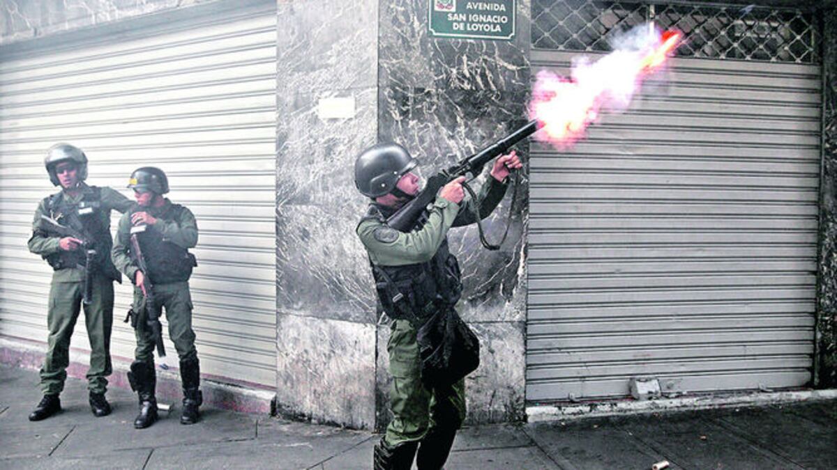 Agentes que reprimían a los manifestantes se resguardan a un costado de un edificio mientras lanzan las bombas lacrimógenas a la multitud.