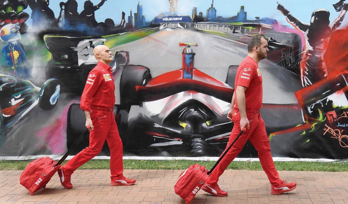 Miembros del equipo Ferrari pasan frente a un cartelón alusivo al Gran Premio de Australia que fue cancelado. AFP